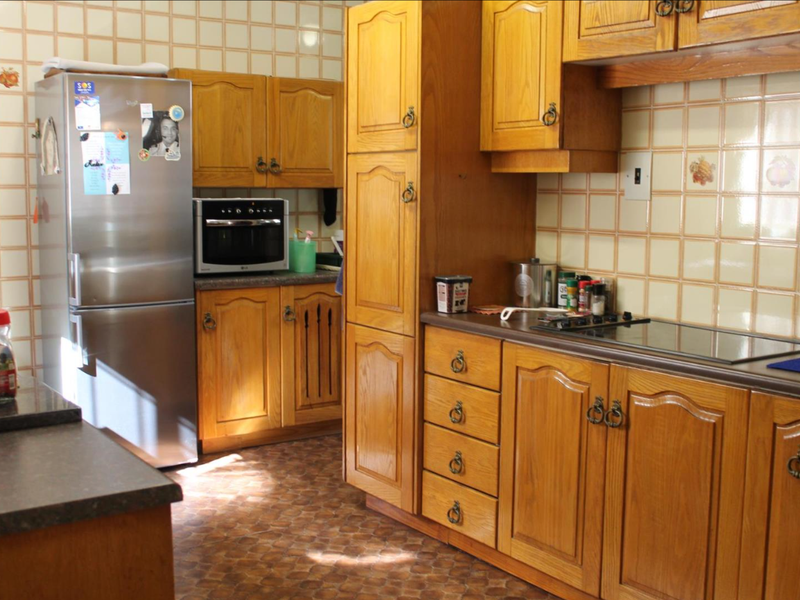 A traditional kitchen featuring wooden cabinetry, laminate countertops, a built-in oven, and an electric hob with tiled backsplash.