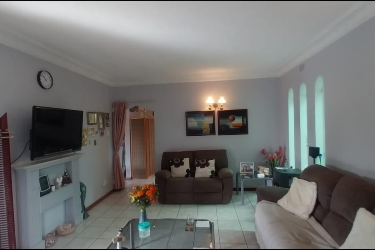 A comfortable living room featuring tiled flooring, coved cornicing, a fireplace mantel, and distinctive arched windows that provide natural light.