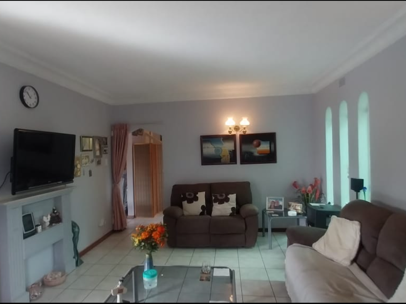 A comfortable living room featuring tiled flooring, coved cornicing, a fireplace mantel, and distinctive arched windows that provide natural light.