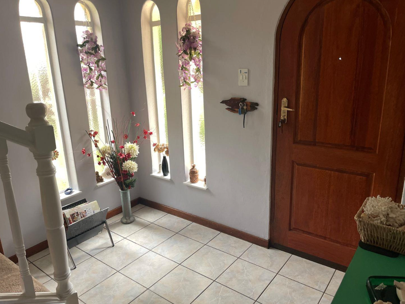 A bright entrance hall featuring tiled flooring, a solid wooden front door, and distinctive arched windows that provide natural light.