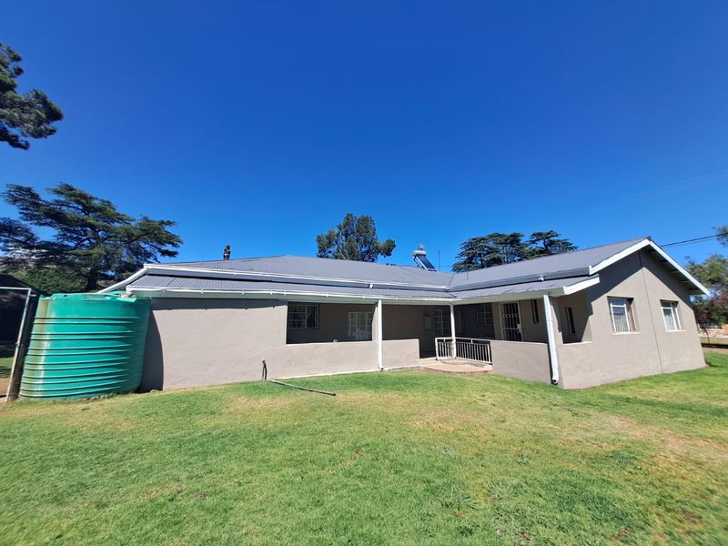Rear view of a single-story house featuring a metal roof, covered patio area, and a large green water storage tank in the garden.