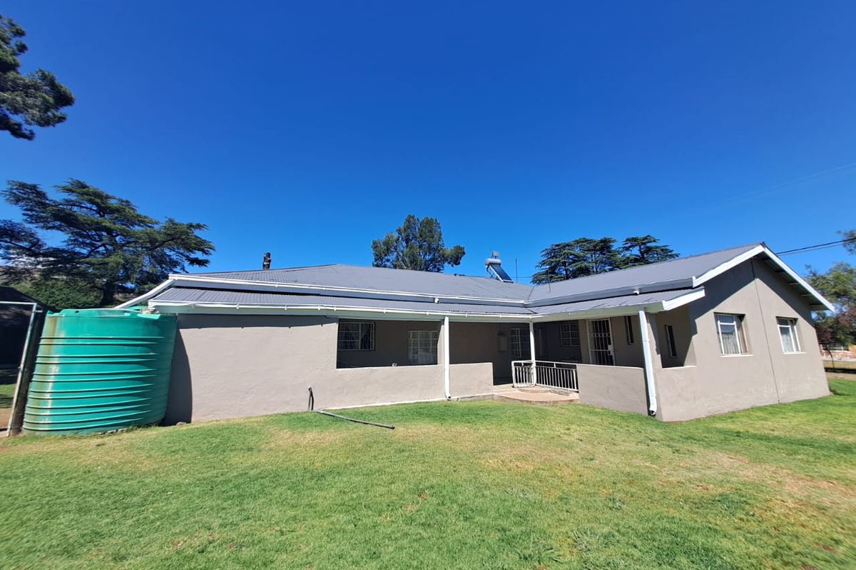 Rear view of a single-story house featuring a metal roof, covered patio area, and a large green water storage tank in the garden.