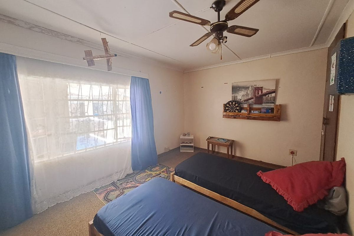 A bedroom featuring a large window with security bars, a ceiling fan, and carpeted flooring.