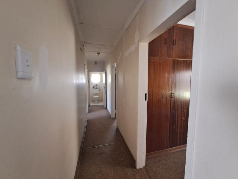 A narrow residential hallway featuring built-in wooden cupboards and carpeted flooring, leading towards a bathroom at the end of the passage.