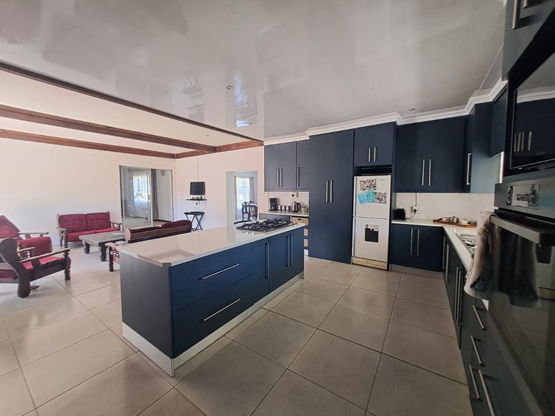Modern open-plan kitchen featuring dark blue cabinetry, a central island with a gas hob, and integrated oven, flowing into the adjacent living area.