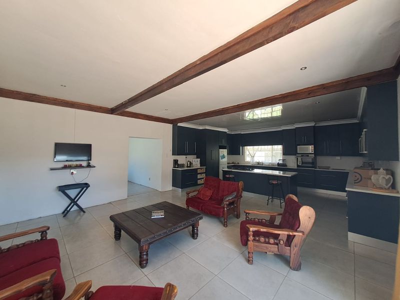 Spacious open-plan living and kitchen area featuring dark cabinetry, a central island, tiled flooring, and exposed timber ceiling beams.
