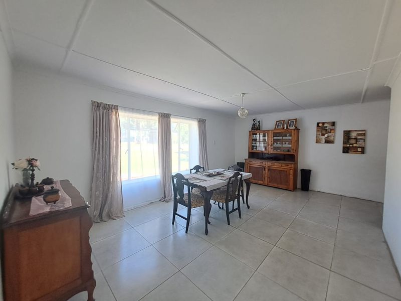 A spacious dining room featuring large windows, neutral tiled flooring, and a simple ceiling finish, offering a bright and functional living space.