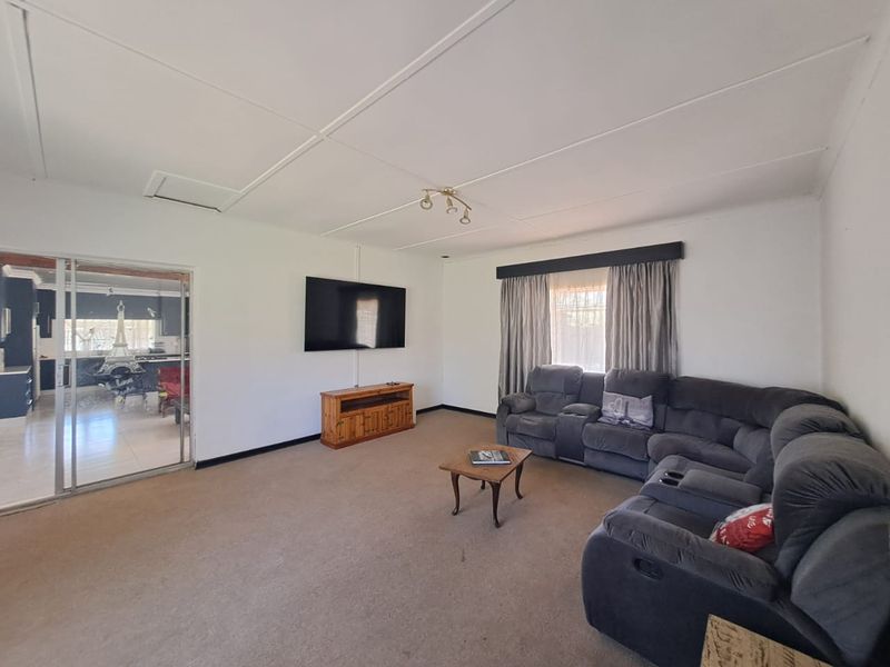 Spacious living room featuring neutral walls, carpeted flooring, and a sliding door providing access to the adjacent kitchen area.