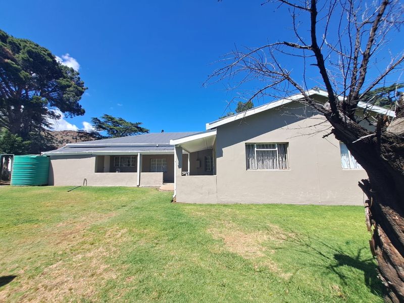 Rear view of the house featuring a covered patio area, metal roof, and a large water storage tank set within a spacious garden.