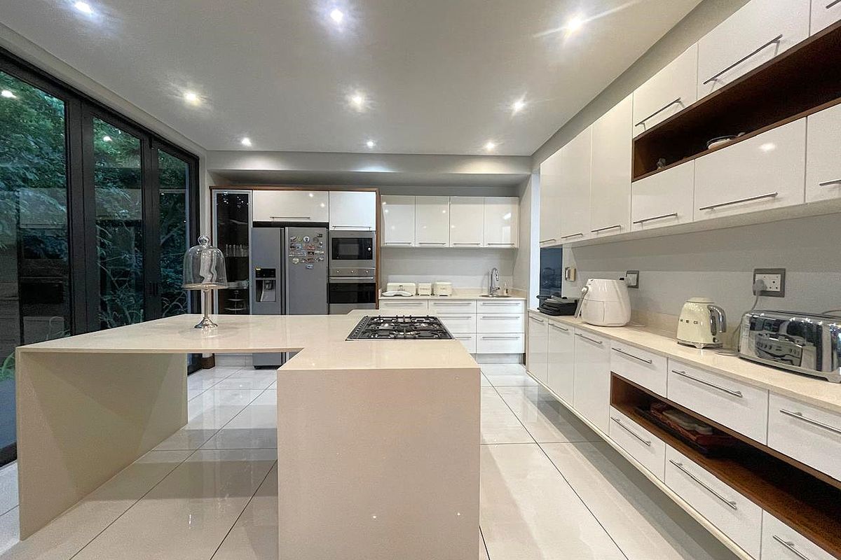 Modern kitchen featuring a large central island with a built-in gas hob, sleek white cabinetry, stone countertops, and recessed ceiling lighting.