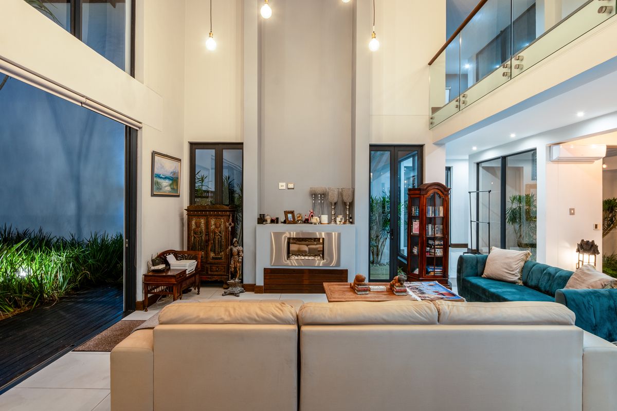 Spacious double-volume living area featuring a modern built-in fireplace, large glass sliding doors, and a mezzanine level with glass balustrades.