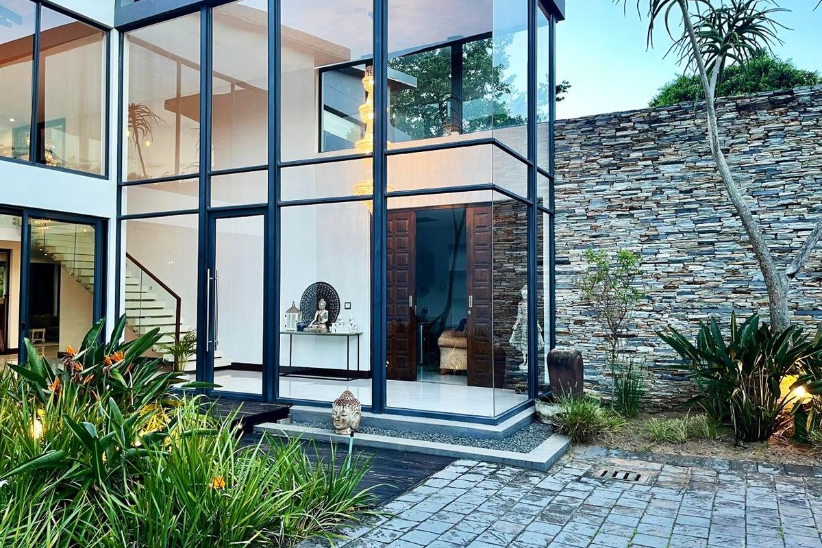 Modern architectural glass-walled entrance foyer featuring double-volume ceilings, stone feature wall, and paved courtyard access.