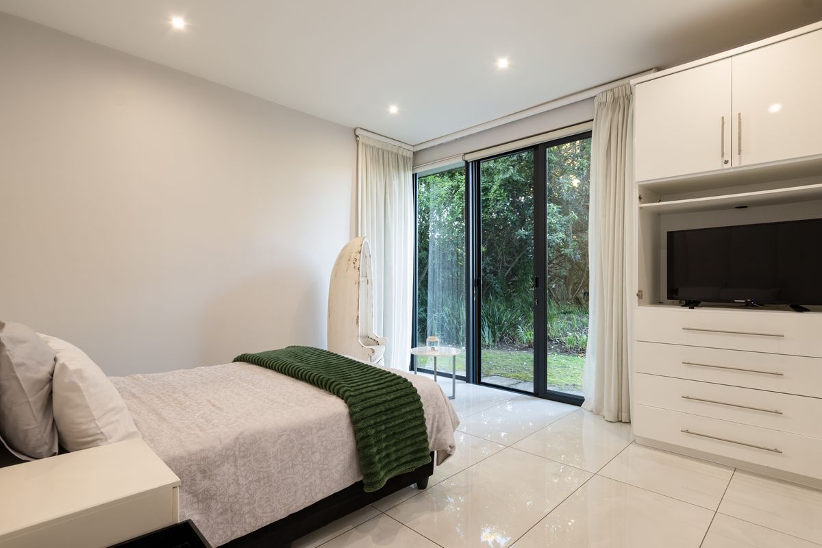 Modern bedroom featuring polished tile flooring, built-in cabinetry, and large sliding glass doors providing direct access to the garden.