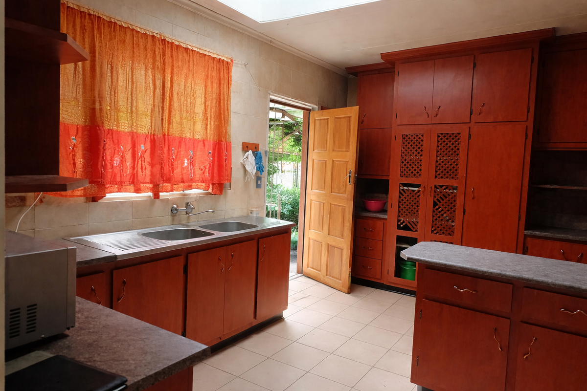 A functional kitchen featuring extensive built-in wooden cabinetry, a double stainless steel sink, tiled flooring, and a skylight providing natural light.