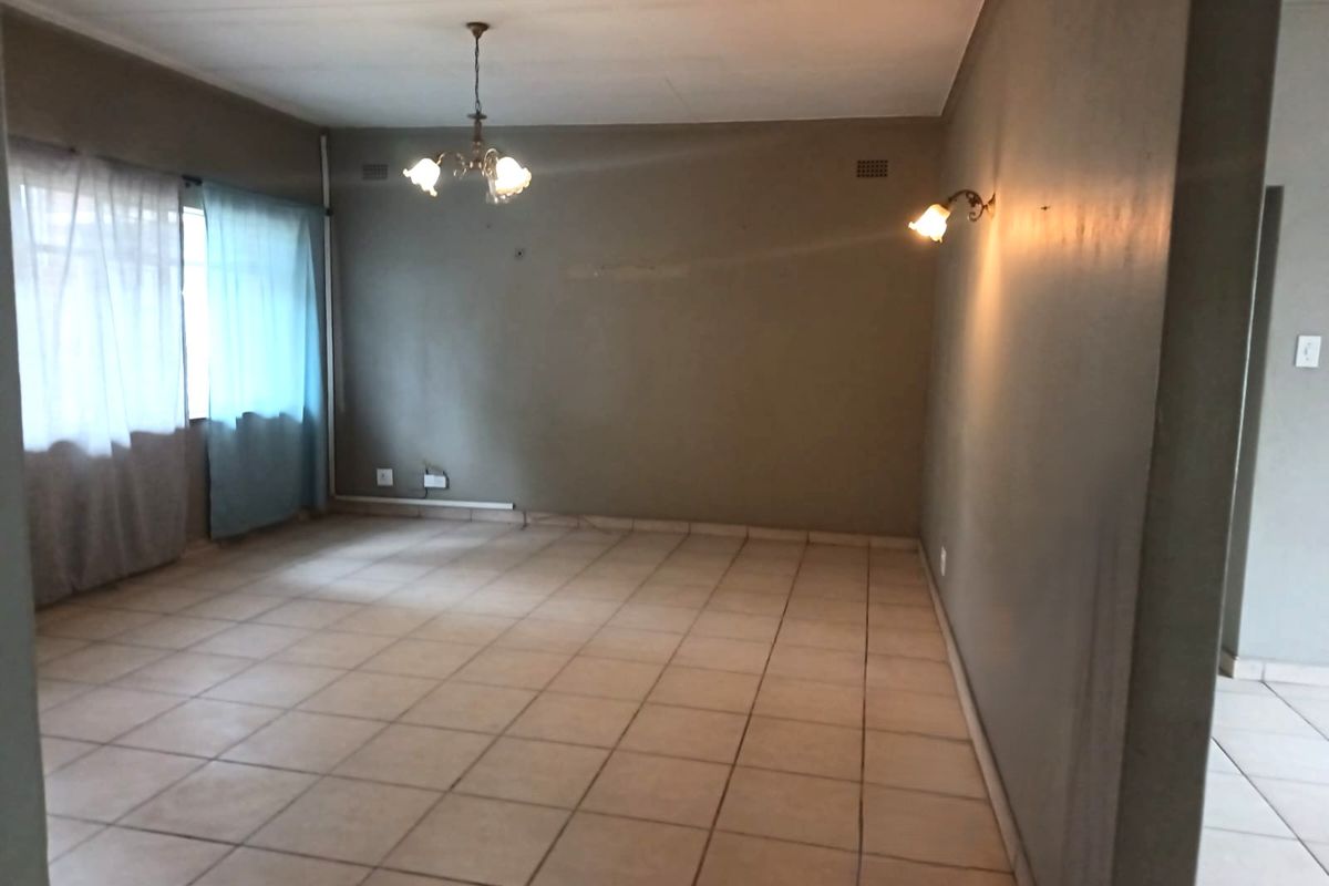An empty living room featuring ceramic floor tiles, a central ceiling light, and wall sconce lighting, providing a blank canvas for interior design.