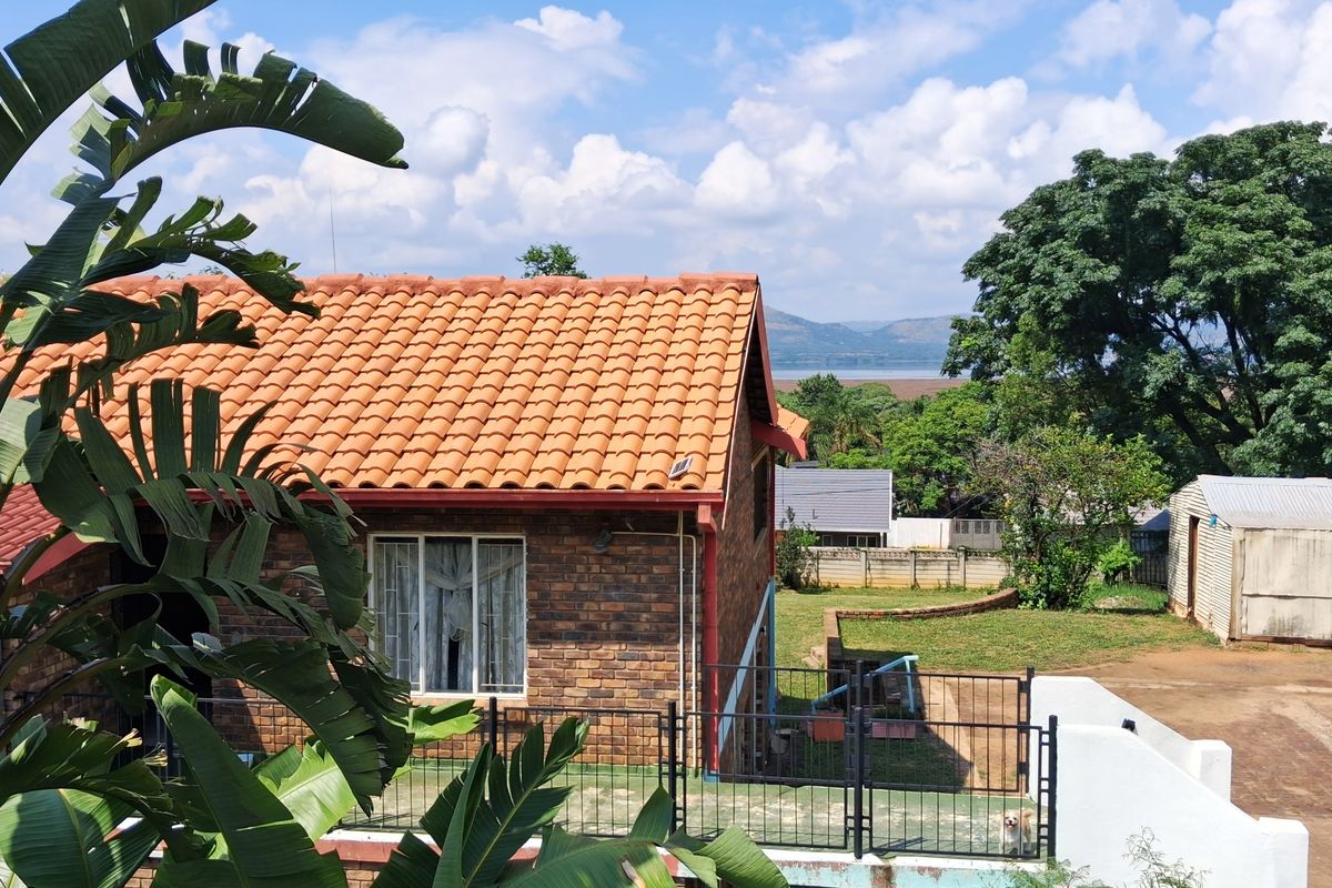 Rear view of a face brick house featuring a terracotta tiled roof, a paved patio area, and surrounding garden space with distant landscape views.