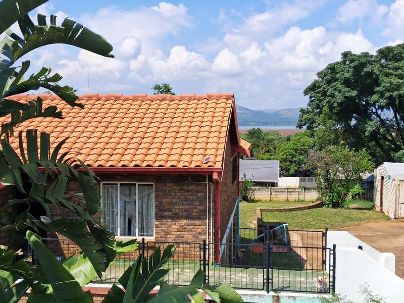 Rear view of a face brick house featuring a terracotta tiled roof, a paved patio area, and surrounding garden space with distant landscape views.