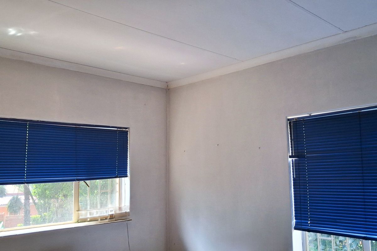 A bright, empty bedroom featuring neutral walls, coving, and blue venetian blinds on the windows.
