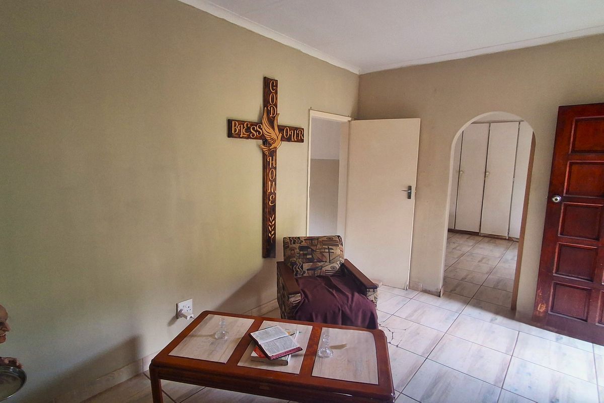 A living area featuring tiled flooring, an arched doorway leading to a bedroom with built-in cupboards, and neutral wall finishes.