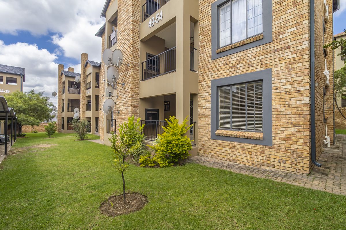 Exterior view of a multi-story apartment complex featuring face-brick facade, private balconies, and landscaped communal garden areas.