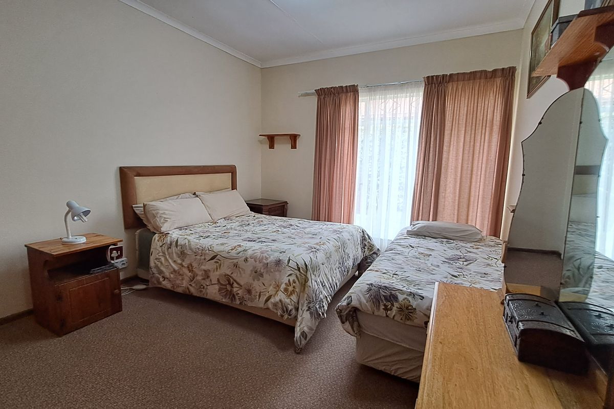 A spacious bedroom featuring carpeted flooring and large windows with curtain rails, offering a functional layout for a primary or guest suite.