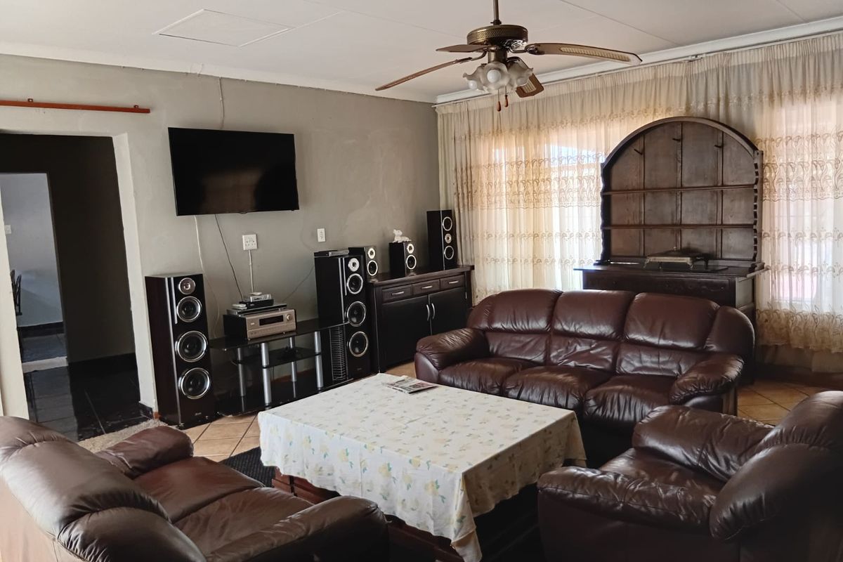 A spacious living room featuring tiled flooring, a ceiling fan, and large windows with curtains, providing a comfortable and functional family living space.