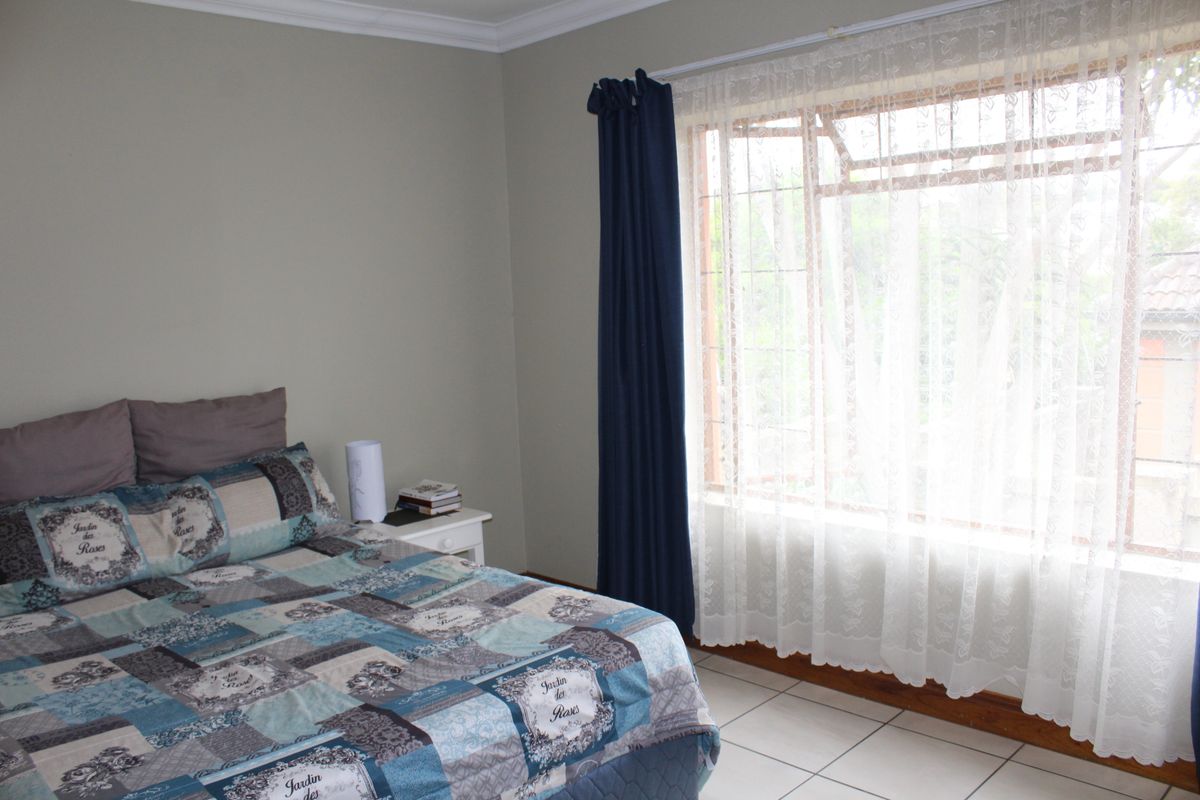 A functional bedroom featuring tiled flooring, a large window with security bars, and coved ceiling cornices.