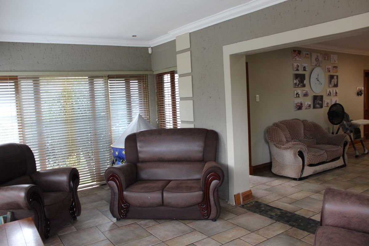 Spacious living area featuring tiled flooring, neutral textured walls, and large windows with fitted venetian blinds, offering a comfortable and functional layout.