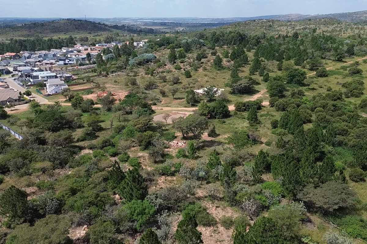 An aerial view of a large, undeveloped residential plot featuring natural vegetation and surrounding suburban housing developments.