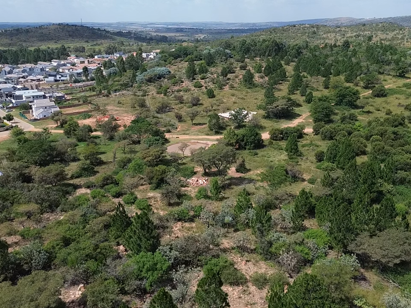An aerial view of a large, undeveloped residential plot featuring natural vegetation and surrounding suburban housing developments.