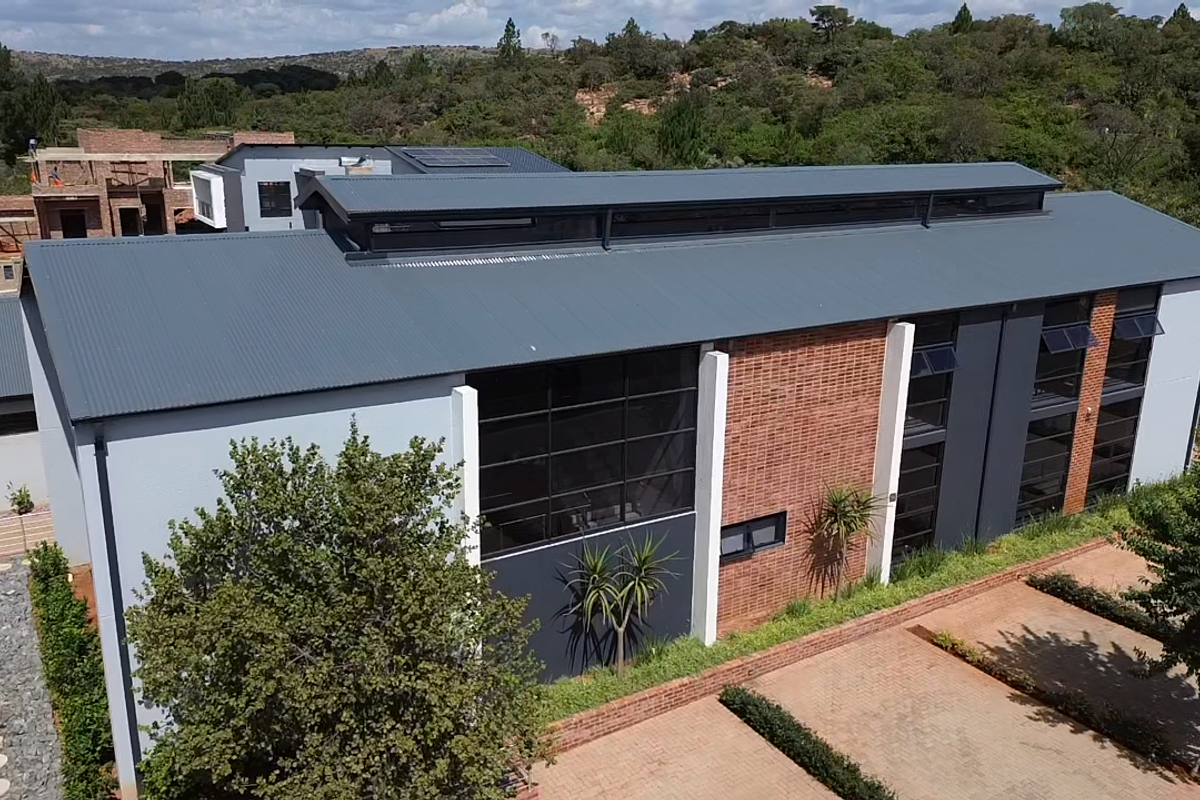 Aerial view of a modern residential property featuring a corrugated metal roof, brick and rendered facade, large windows, and a paved driveway.