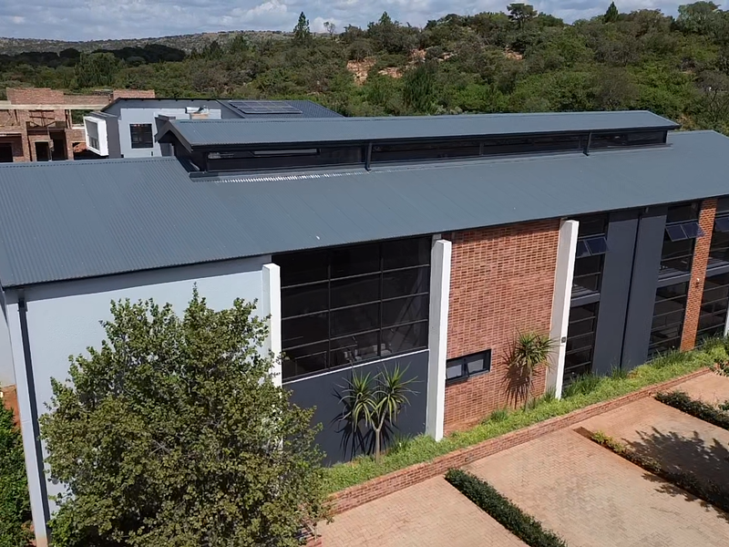 Aerial view of a modern residential property featuring a corrugated metal roof, brick and rendered facade, large windows, and a paved driveway.
