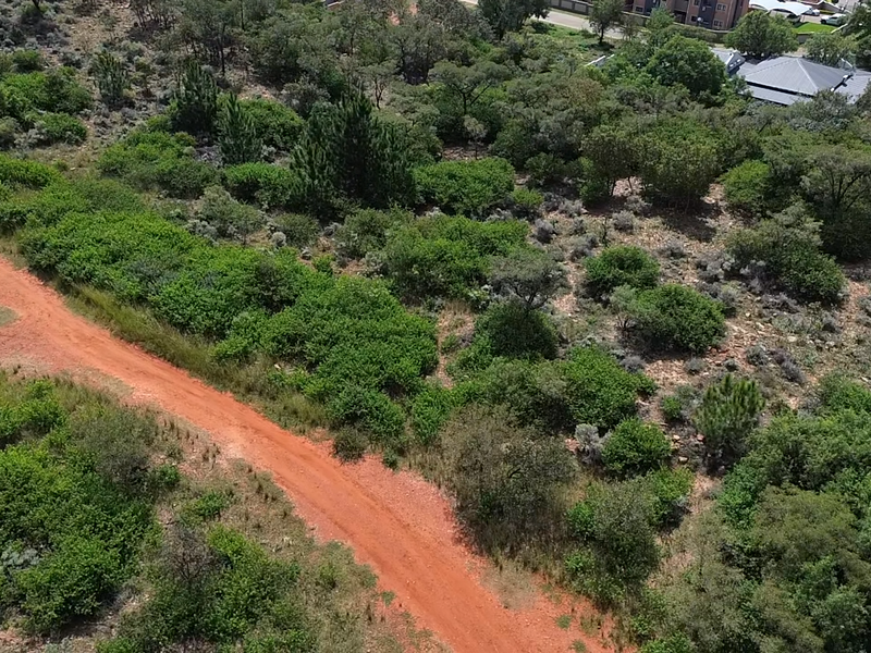An aerial view of a vacant residential plot featuring natural vegetation and an unpaved access road.