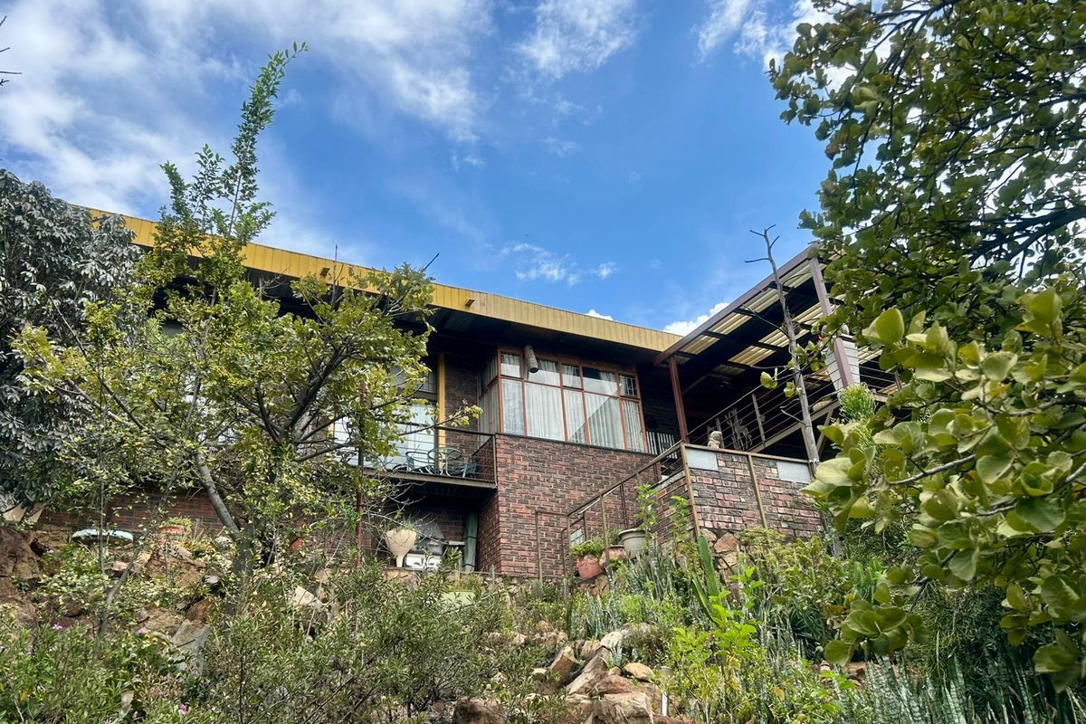 Rear view of a multi-level brick house featuring a covered patio area and established terraced garden landscaping.