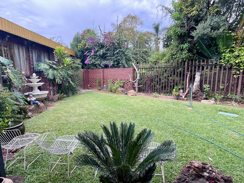 A well-maintained rear garden featuring a lush lawn, stone patio area, brick boundary walls, and established perimeter security fencing.