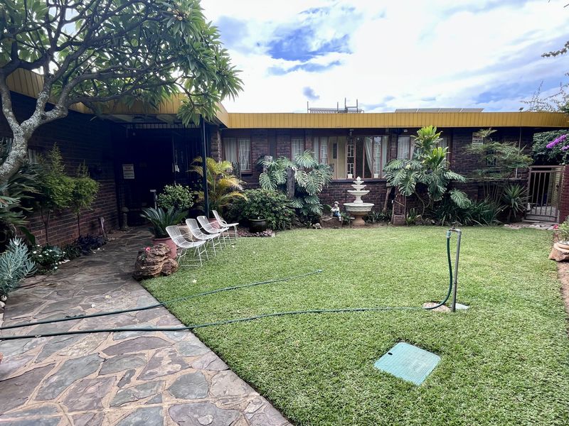 A private rear garden featuring a stone-paved patio area, a well-maintained lawn, and a decorative water fountain set against a brick building facade.