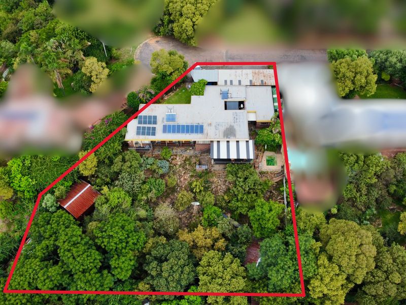 Aerial view of the property showing the main dwelling with solar panels, a swimming pool, and extensive surrounding garden area.