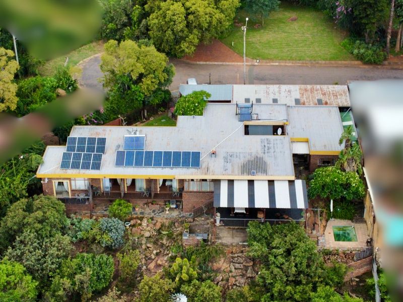 Aerial view of a residential property featuring a corrugated metal roof with solar panels, a rear patio, and a swimming pool set in a garden.