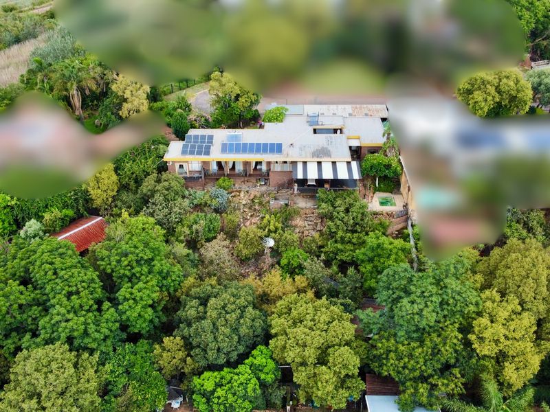 Aerial view of a residential property nestled in a lush, tree-filled garden, featuring solar panels on the roof and a covered patio area.
