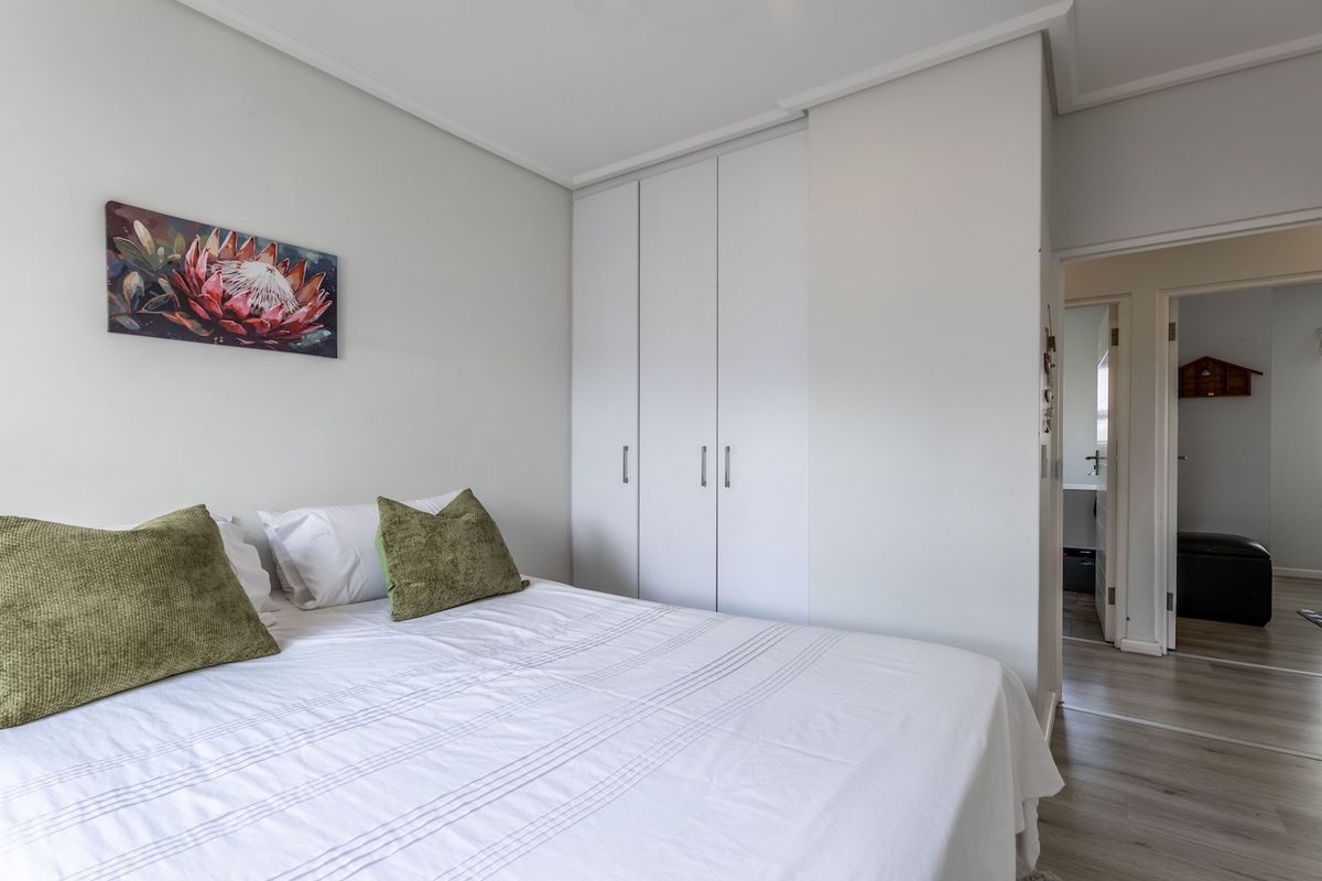 A bright bedroom featuring built-in cupboards, neutral wall finishes, and light-toned laminate flooring, with an adjacent doorway leading to an adjoining room.