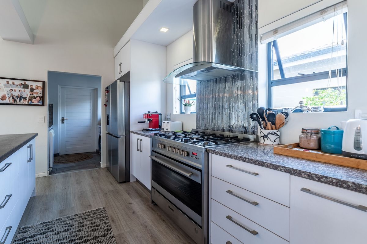 Modern kitchen featuring white cabinetry, granite countertops, stainless steel gas stove with extractor fan, and a decorative tiled backsplash.