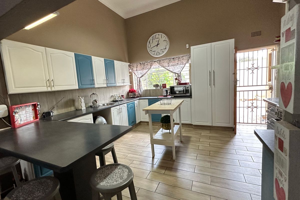 Spacious kitchen featuring two-tone cabinetry, laminate countertops, tiled flooring, and direct access to the exterior via a security gate.