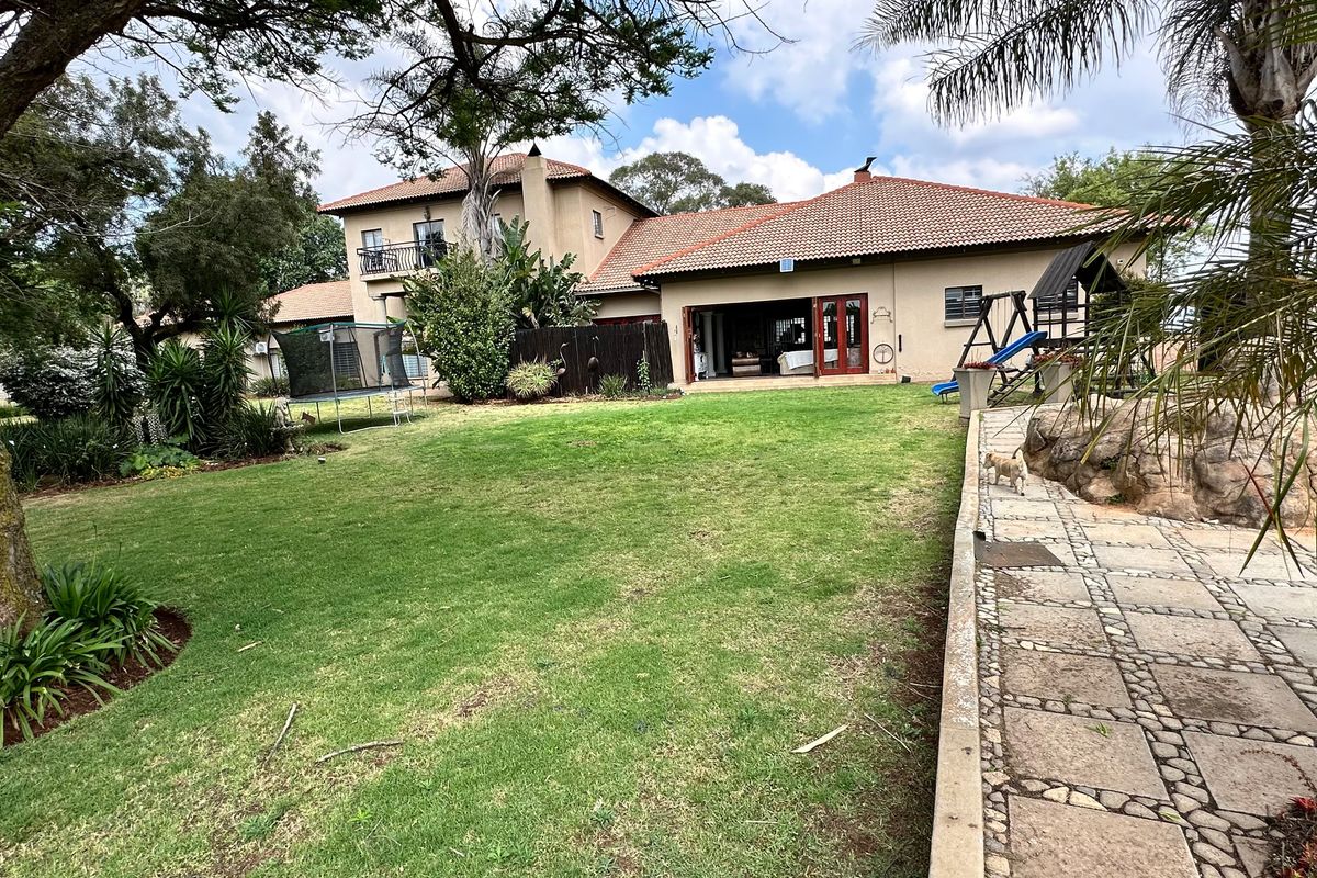 Rear view of a multi-story residence featuring a spacious lawn, stone-paved pathway, and a covered patio area with double door access.