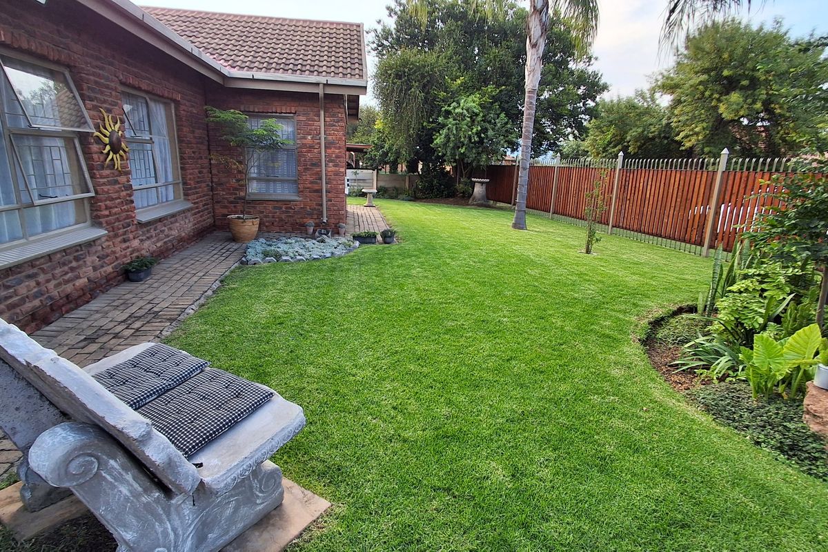 A well-maintained rear garden featuring a lush green lawn, paved walkway, and secure timber fencing along the property boundary.