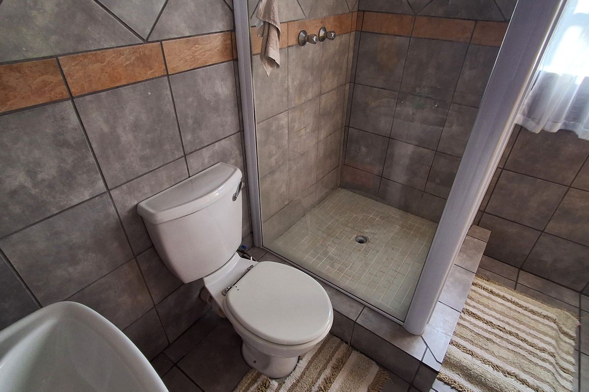 A functional bathroom featuring a tiled shower enclosure and a standard toilet with neutral wall and floor tiling.