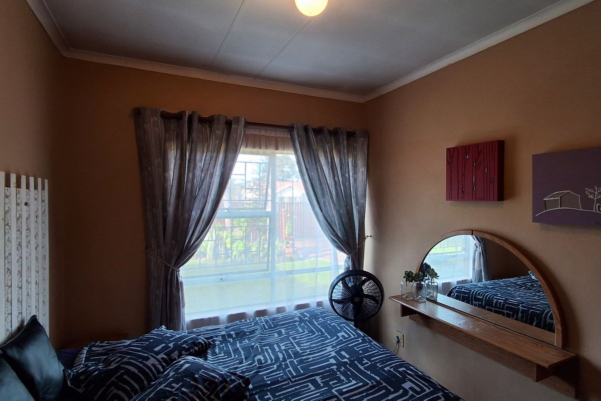 A cozy bedroom featuring a window with security bars, a wall-mounted mirror, and a built-in shelf.