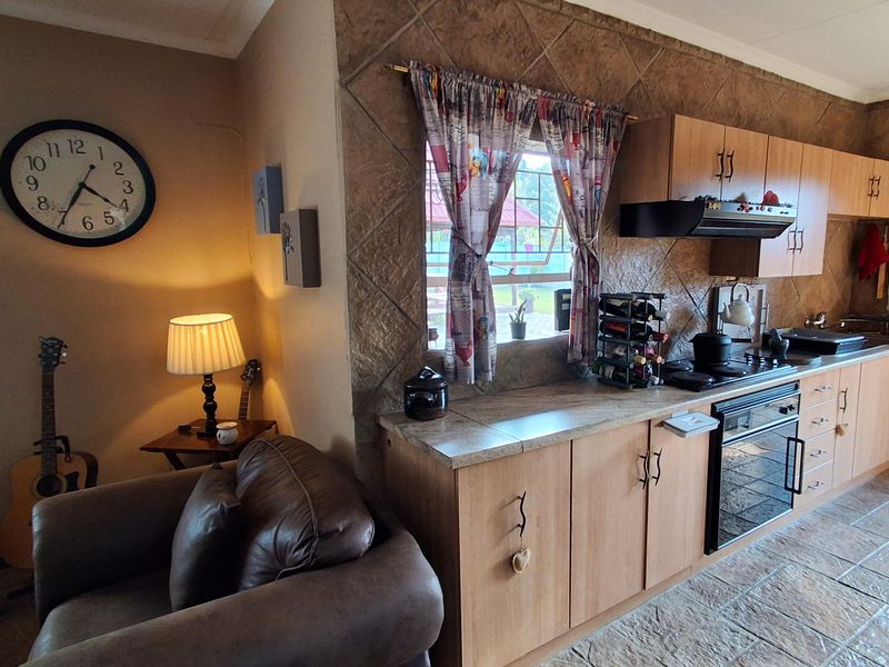Open-plan kitchen area featuring wood-finish cabinetry, tiled countertops, and a tiled feature wall, seamlessly integrated with the adjacent living space.