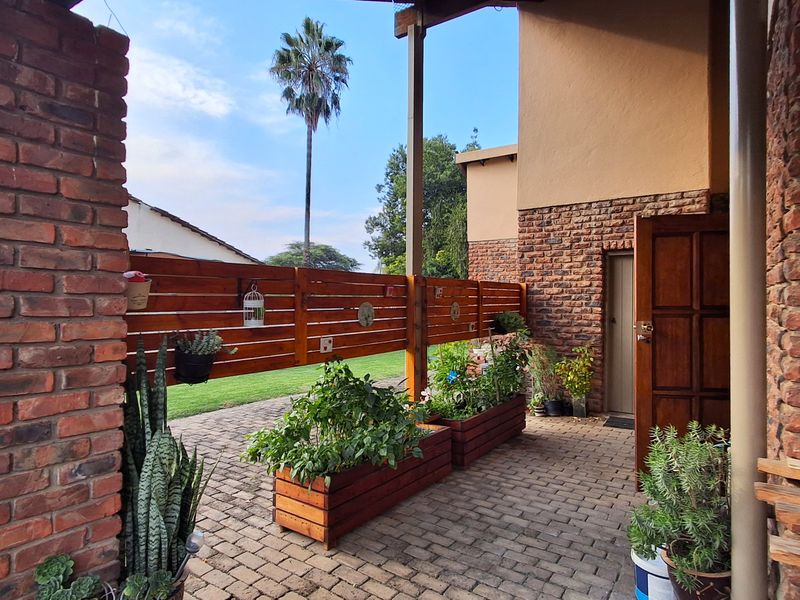 A covered patio area featuring brick paving, exposed brick walls, and a timber privacy screen overlooking the garden.