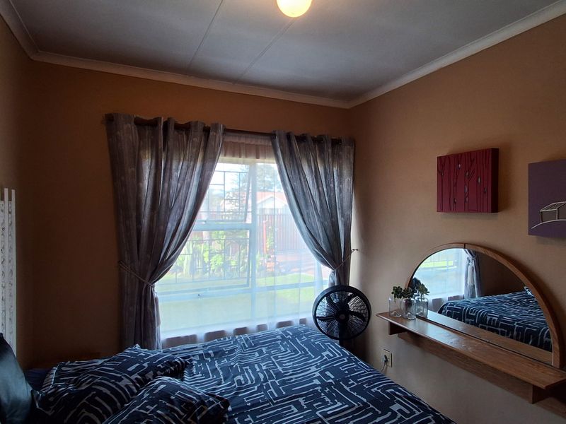A cozy bedroom featuring a window with security bars, a wall-mounted mirror, and a built-in shelf.
