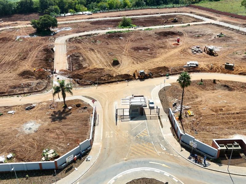 Aerial view of a residential development site showing the security entrance, internal road network, and cleared plots ready for construction.